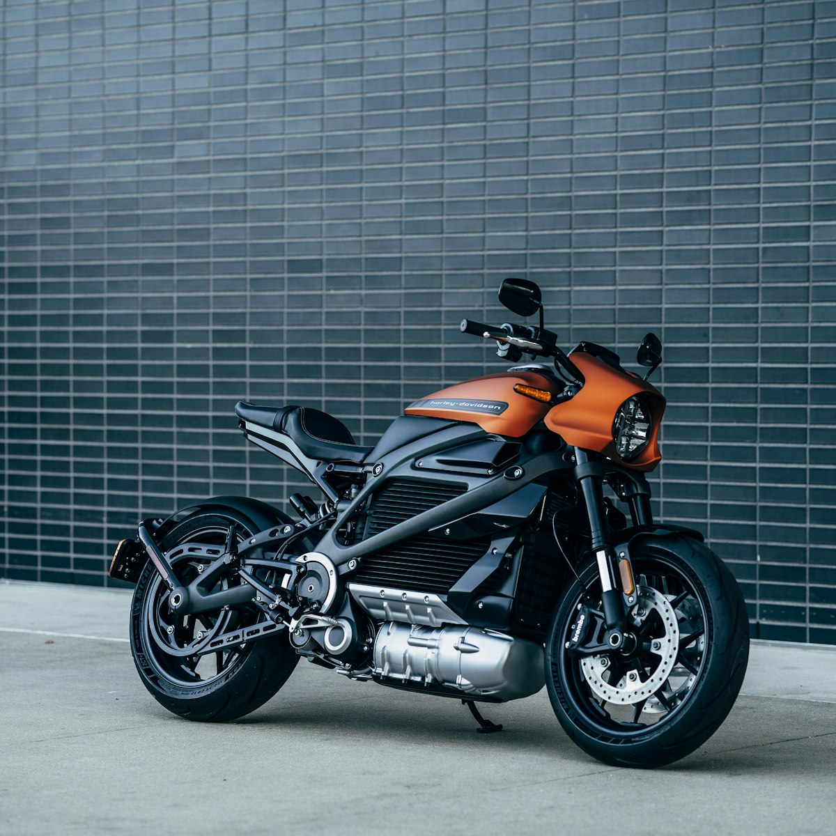 Orange motorcycle parked against a dark brick wall